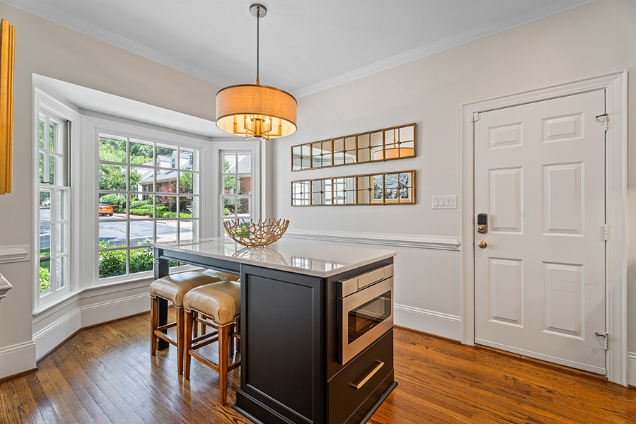 Renovated Dining Area in Kitchen. Shows an island with stools surrounding it inside of large front window.